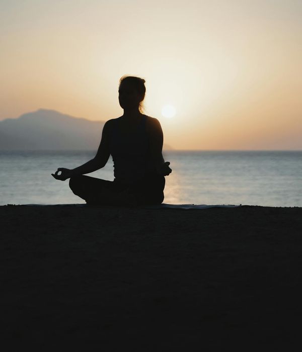 Woman in a calm yoga pose on a beach during sunset.